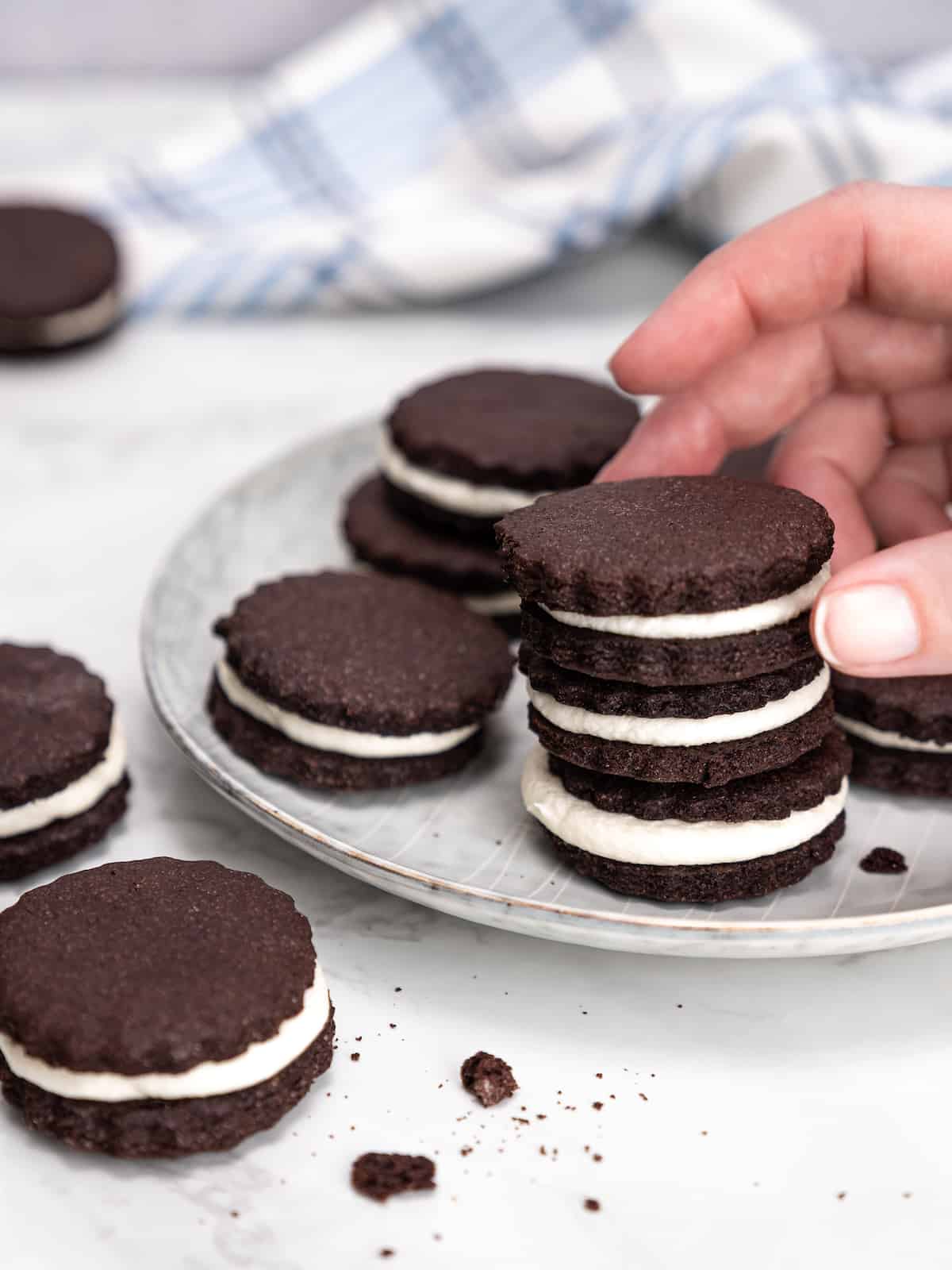 A hand picks up a homemade Oreo from a stack of sandwich cookies on a plate.