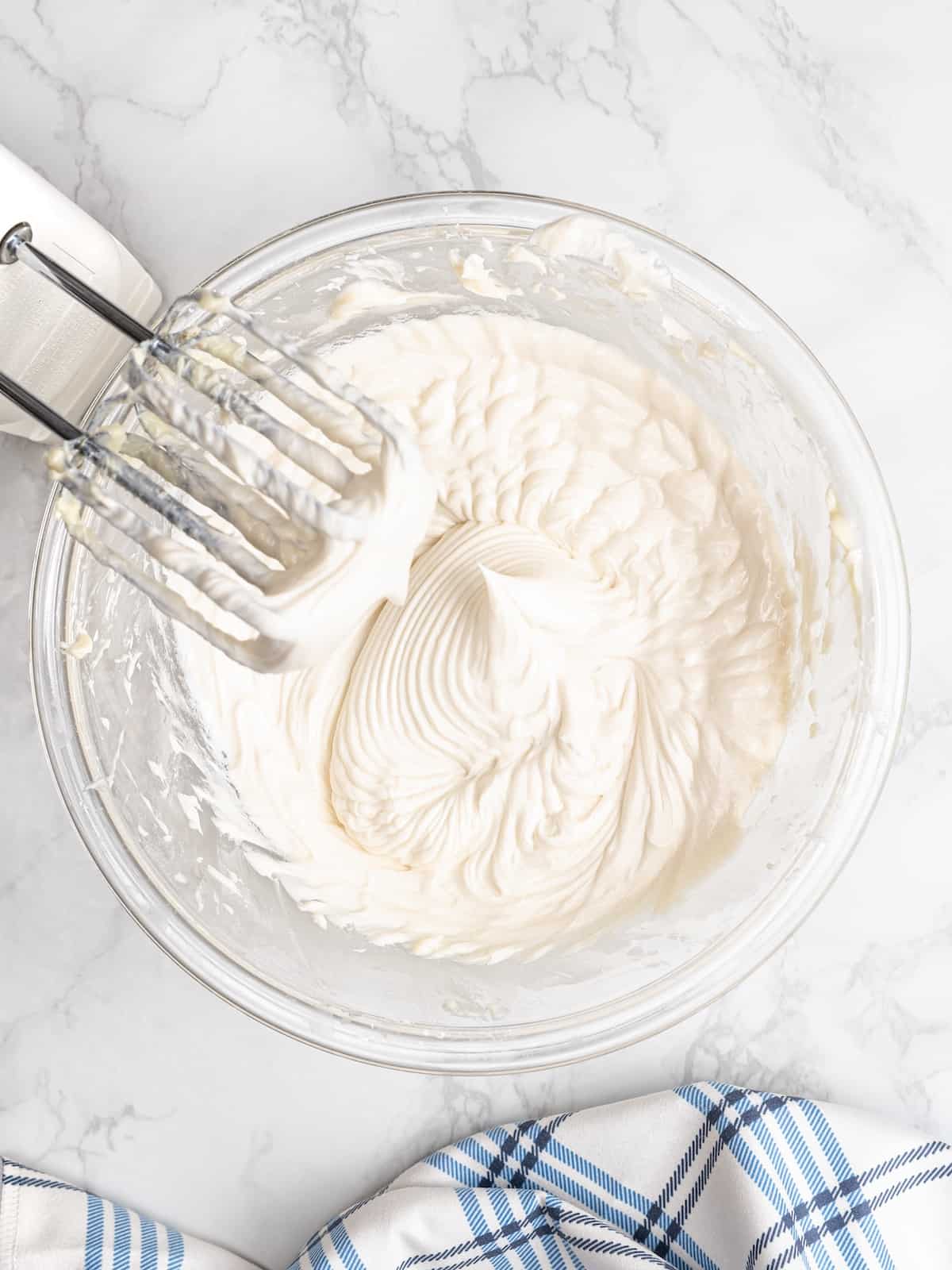 A hand mixer propped over a bowl with freshly beaten vanilla cream filling.