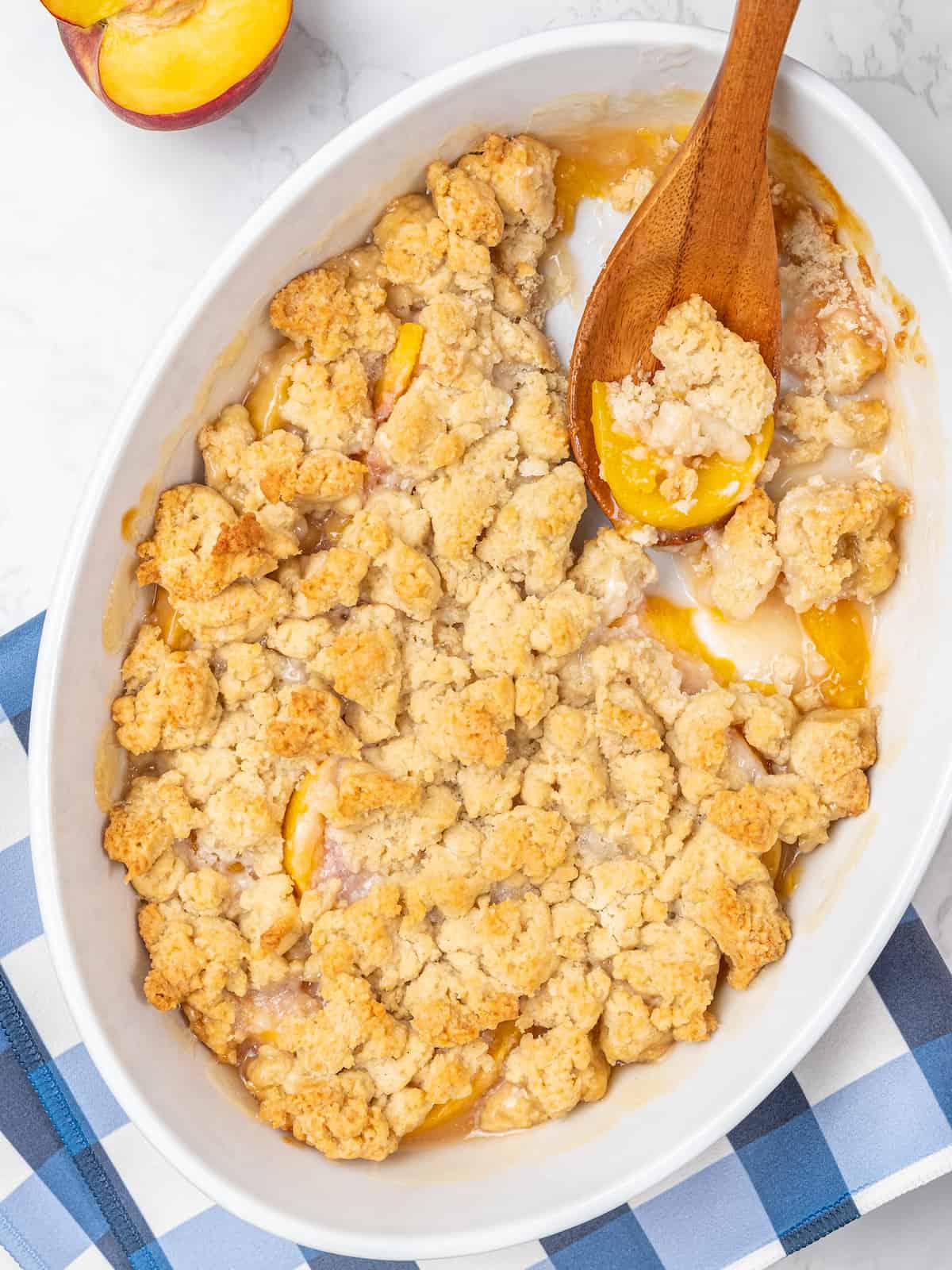 Baked gluten free peach cobbler in an oval dish, with a wooden spoon for serving.