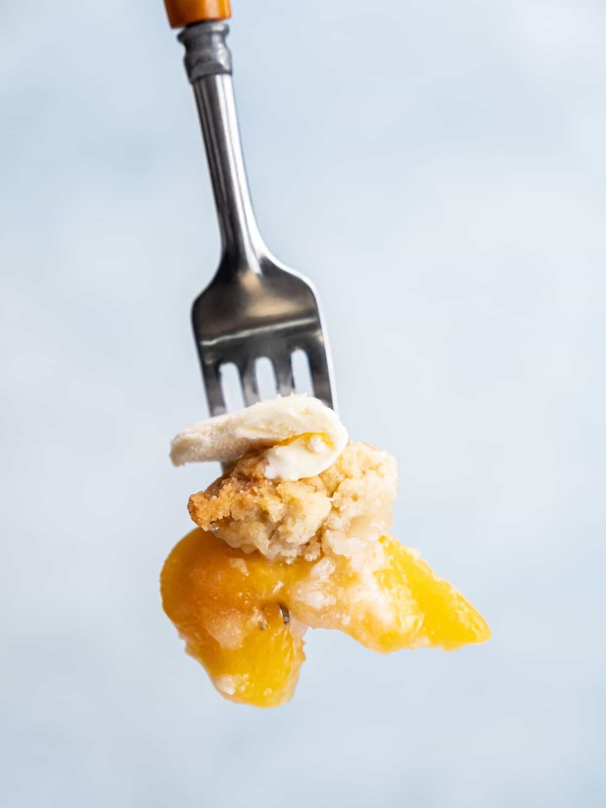 Close up of a forkful of gluten free peach cobbler.