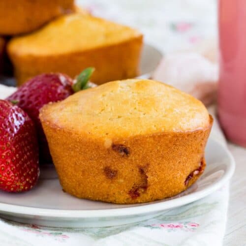 A strawberry muffin on a small white plate with some fresh strawberries.