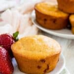 A strawberry muffin on a plate with fresh strawberries and more muffins in a dish behind it.