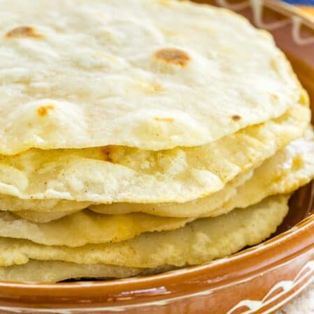 Gluten free tortillas stacked in a brown bowl with a colorful striped cloth in the background.