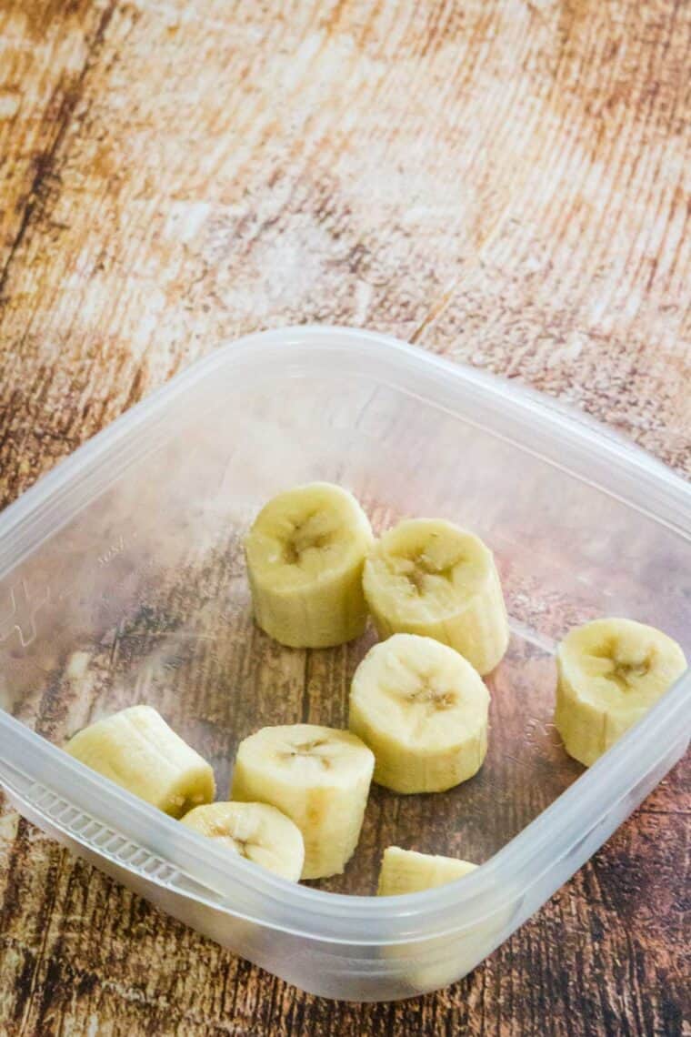 A freezer-safe container sitting open on the table with banana slices in it