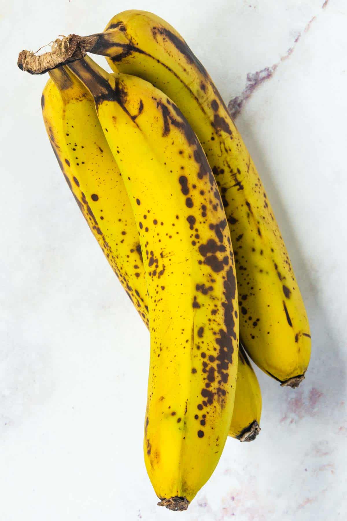 A bunch of three slightly spotted bananas sitting on the countertop