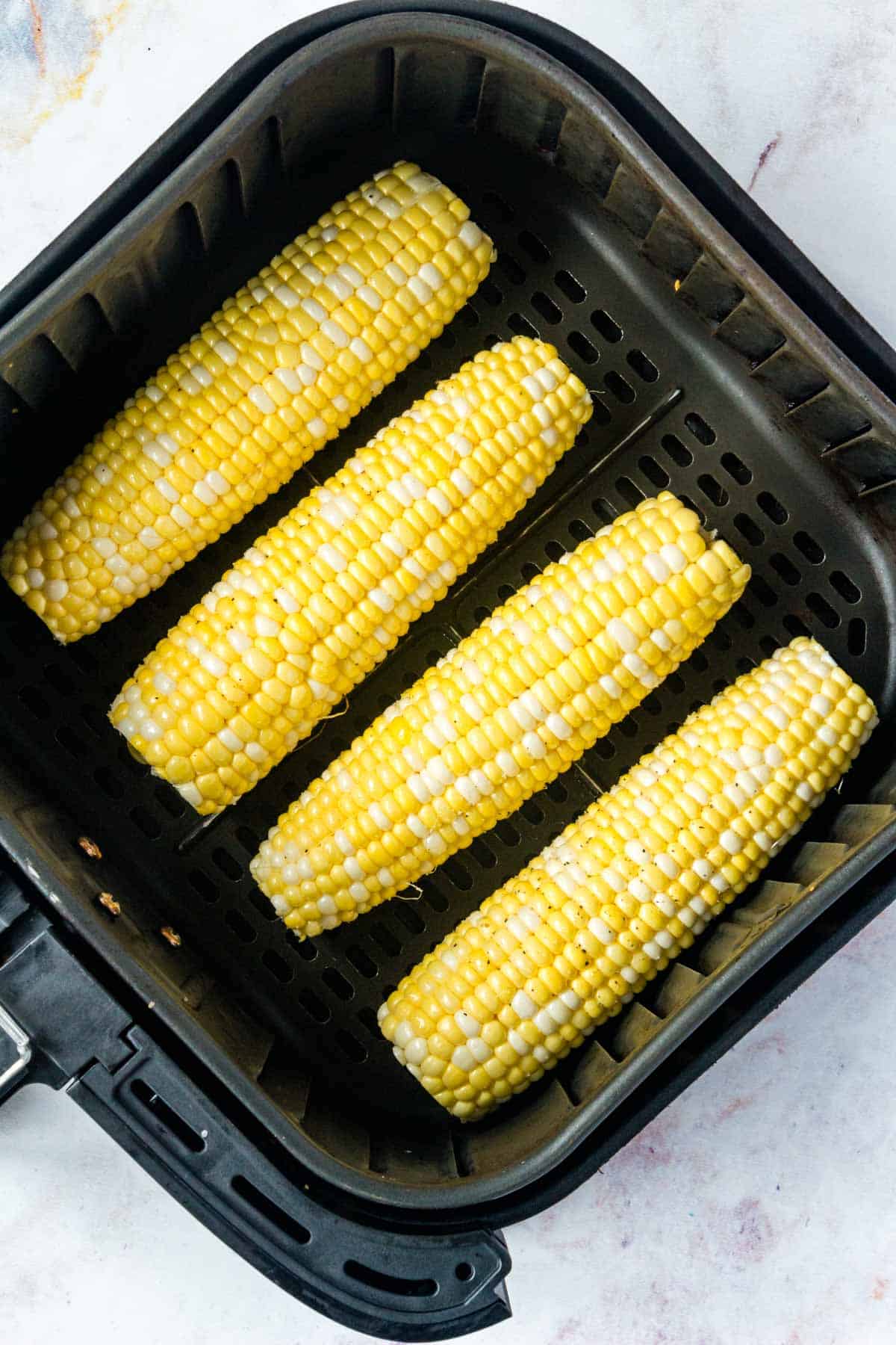 Top view of seasoned corn on the cob inside the air fryer.