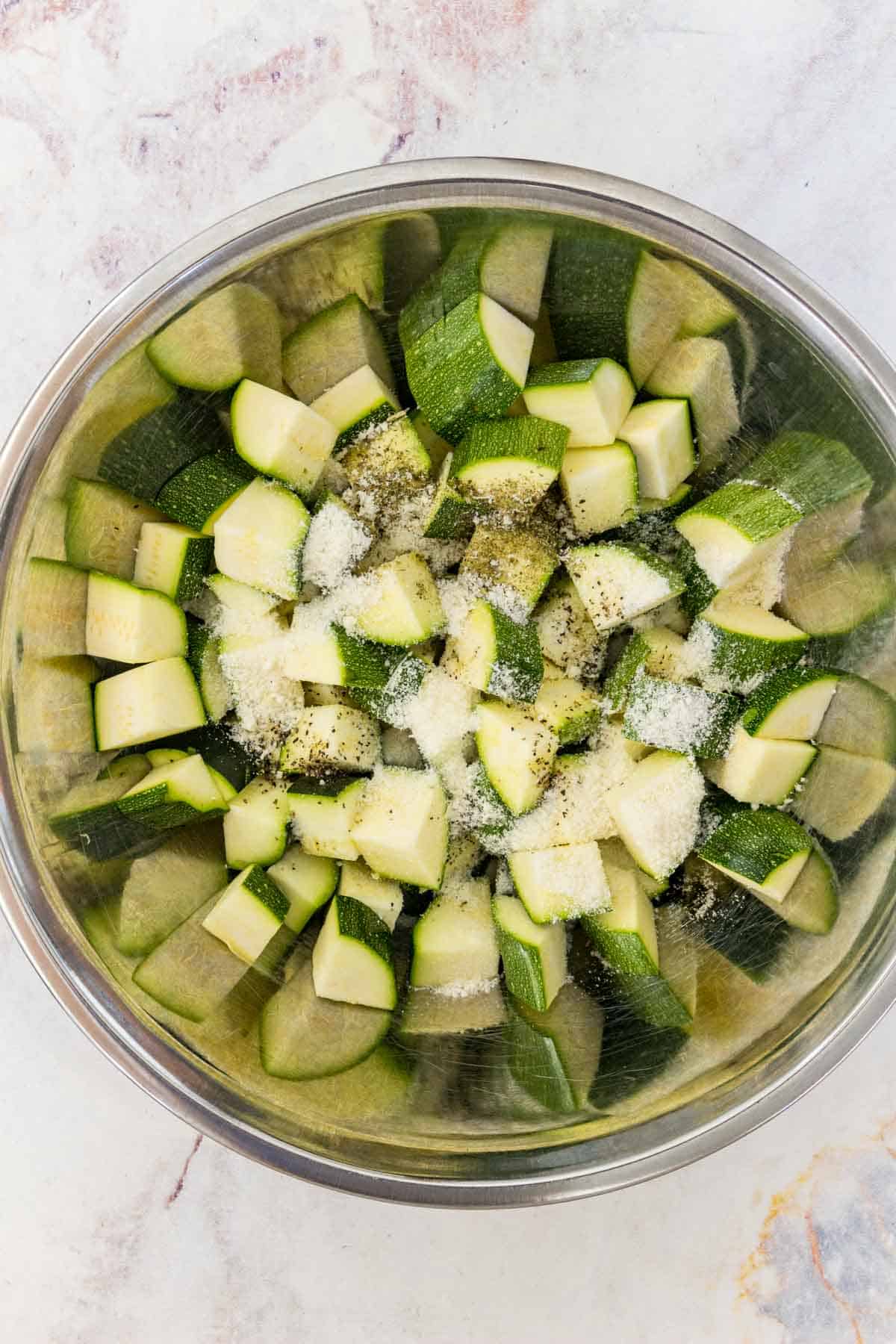 Parmesan and seasonings are added into a bowl with chunks of chopped zucchini.