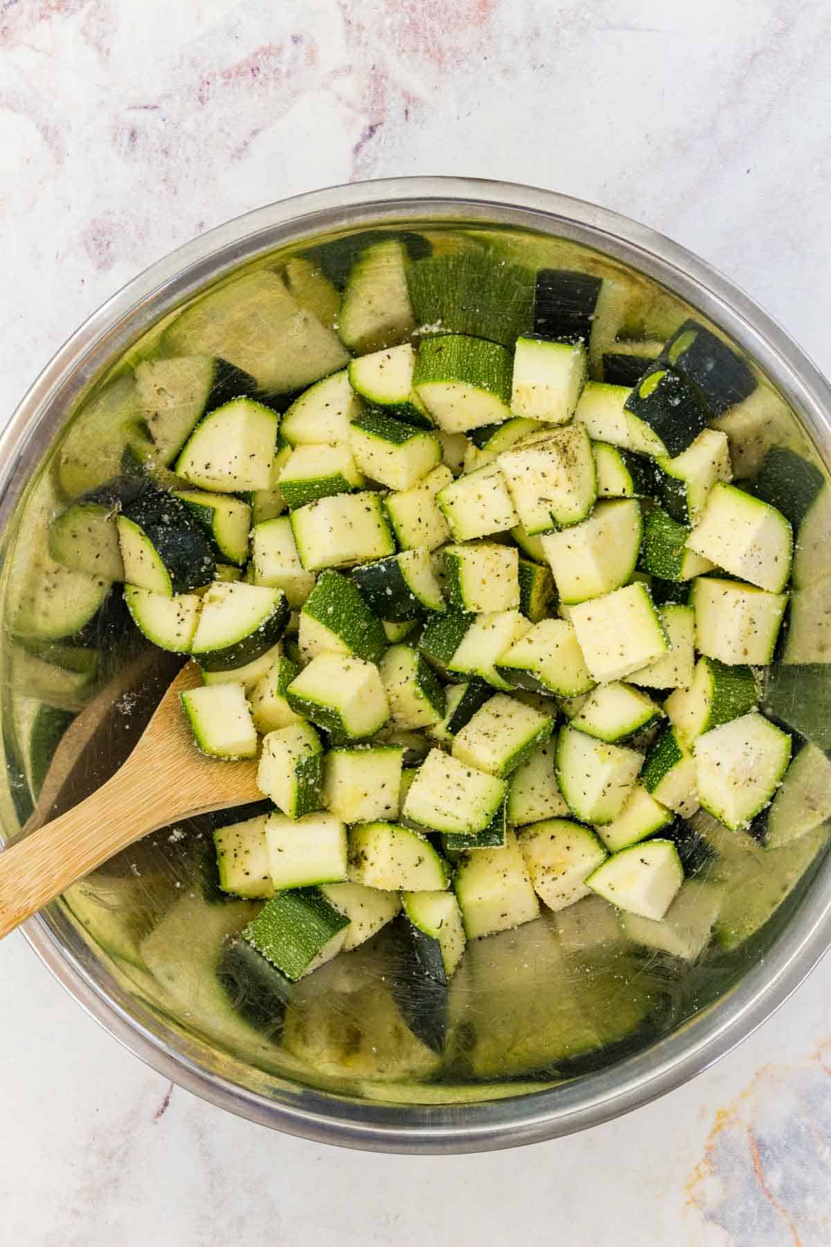 Zucchini is tossed in a coating of olive oil, parmesan, and seasoning in a mixing bowl.