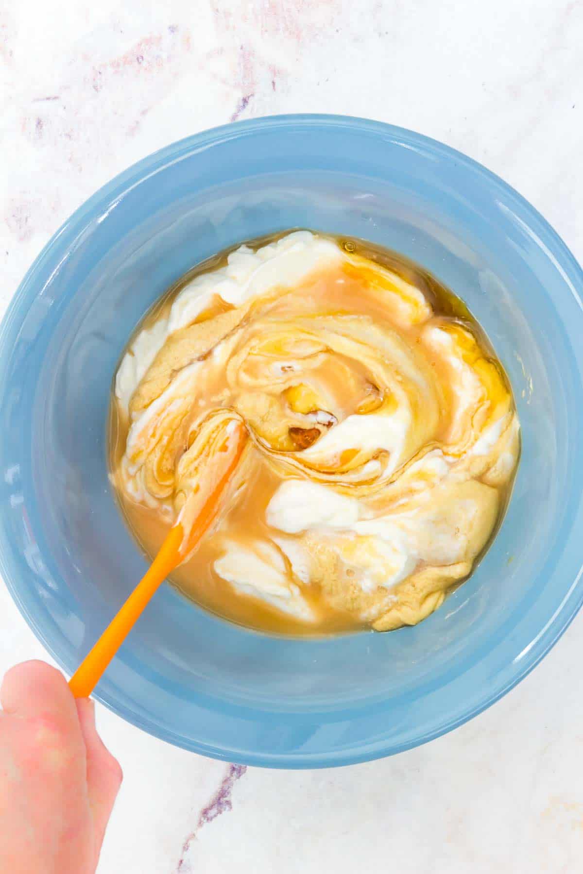 Stirring the dressing together in a blue bowl with a spatula.