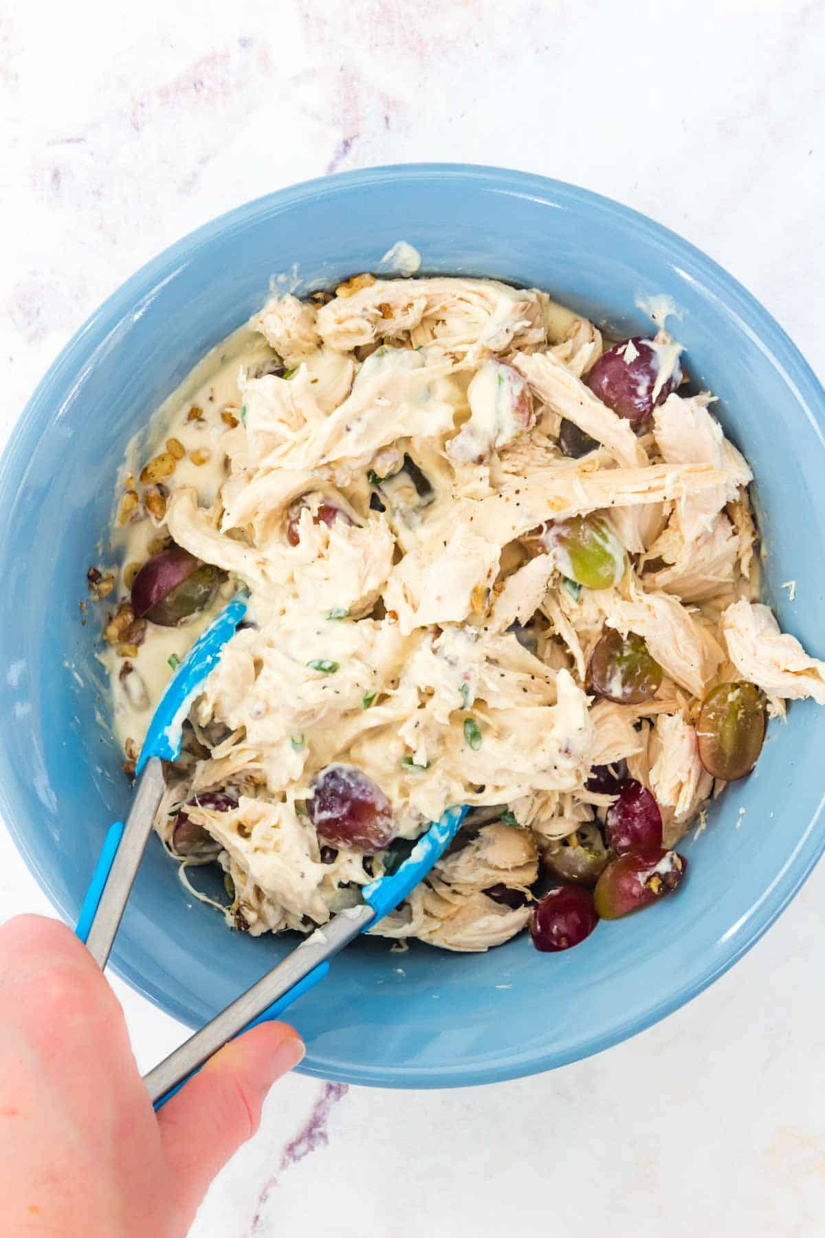 Tossing the chicken salads with grapes and walnuts using tongs.
