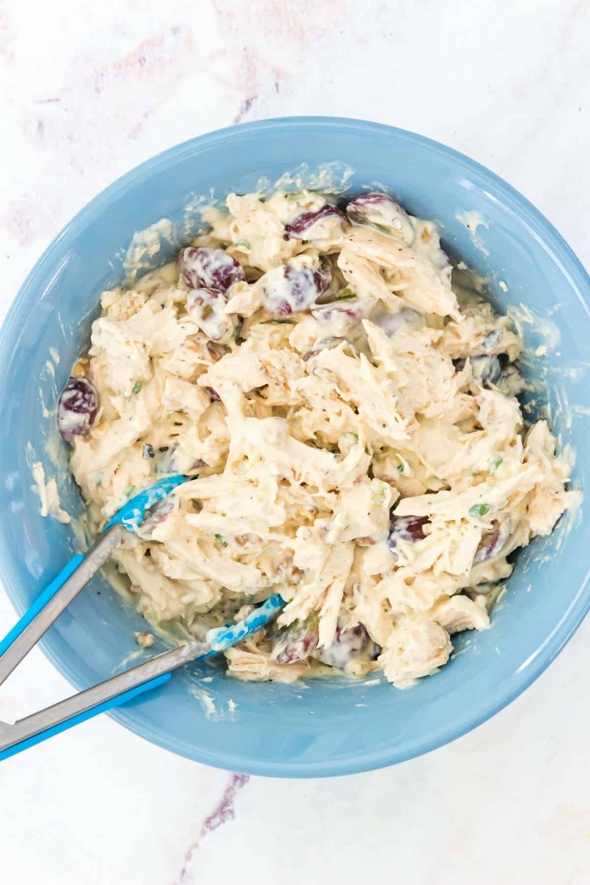 Tongs in a blue bowl of chicken salad.