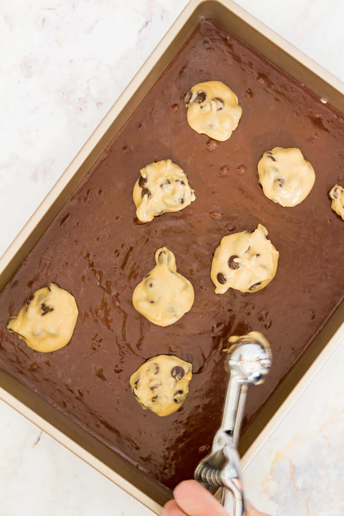 Cookie dough is dropped over the brownie batter in a large rectangular baking pan.