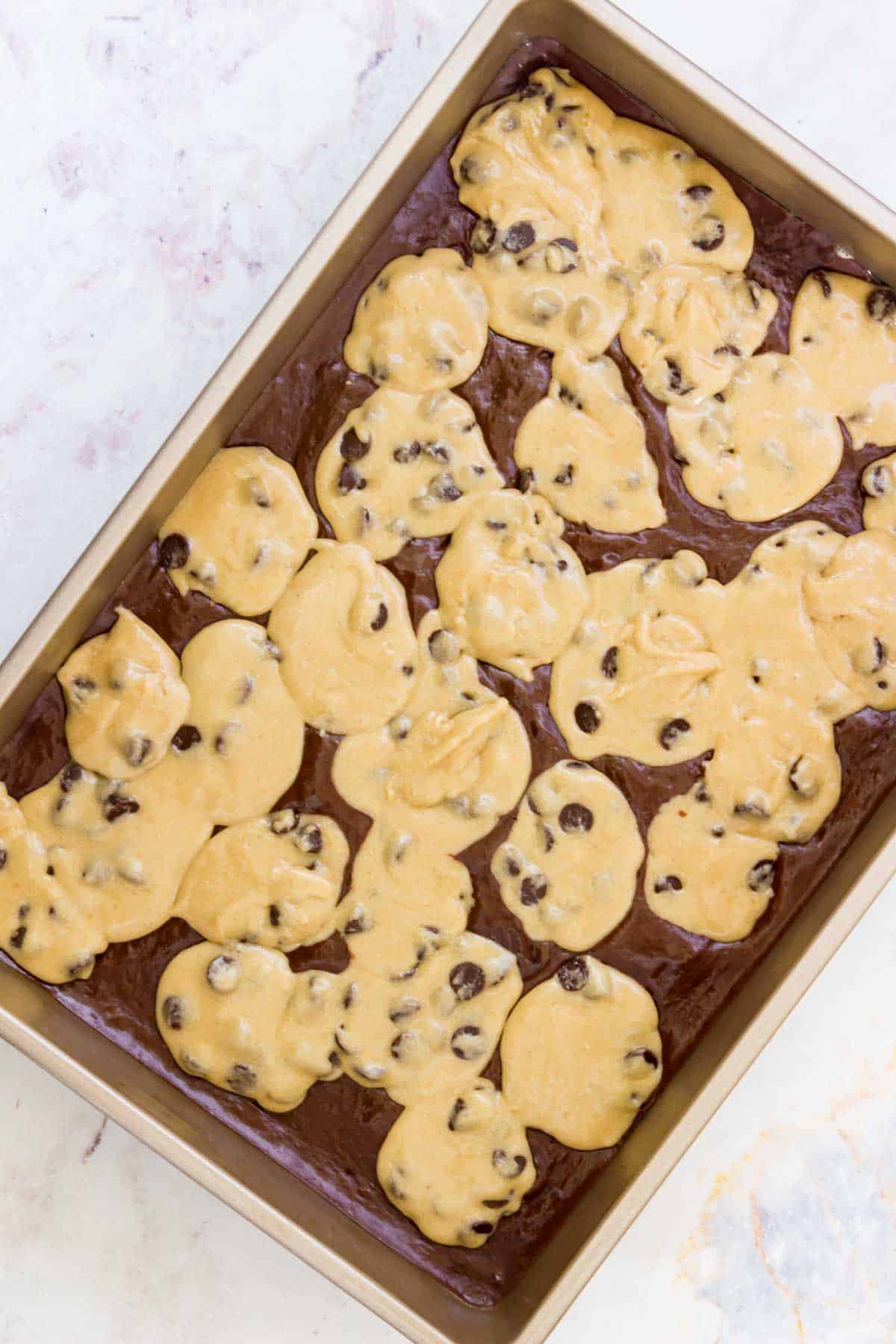Cookie dough and brownie batter in a rectangular baking pan, ready to be baked.