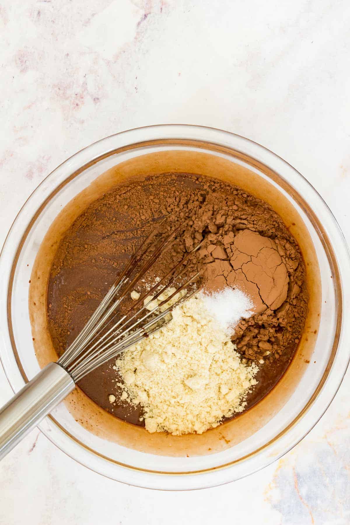 Dry ingredients are whisked into a mixing bowl with the wet ingredients for brownie batter.