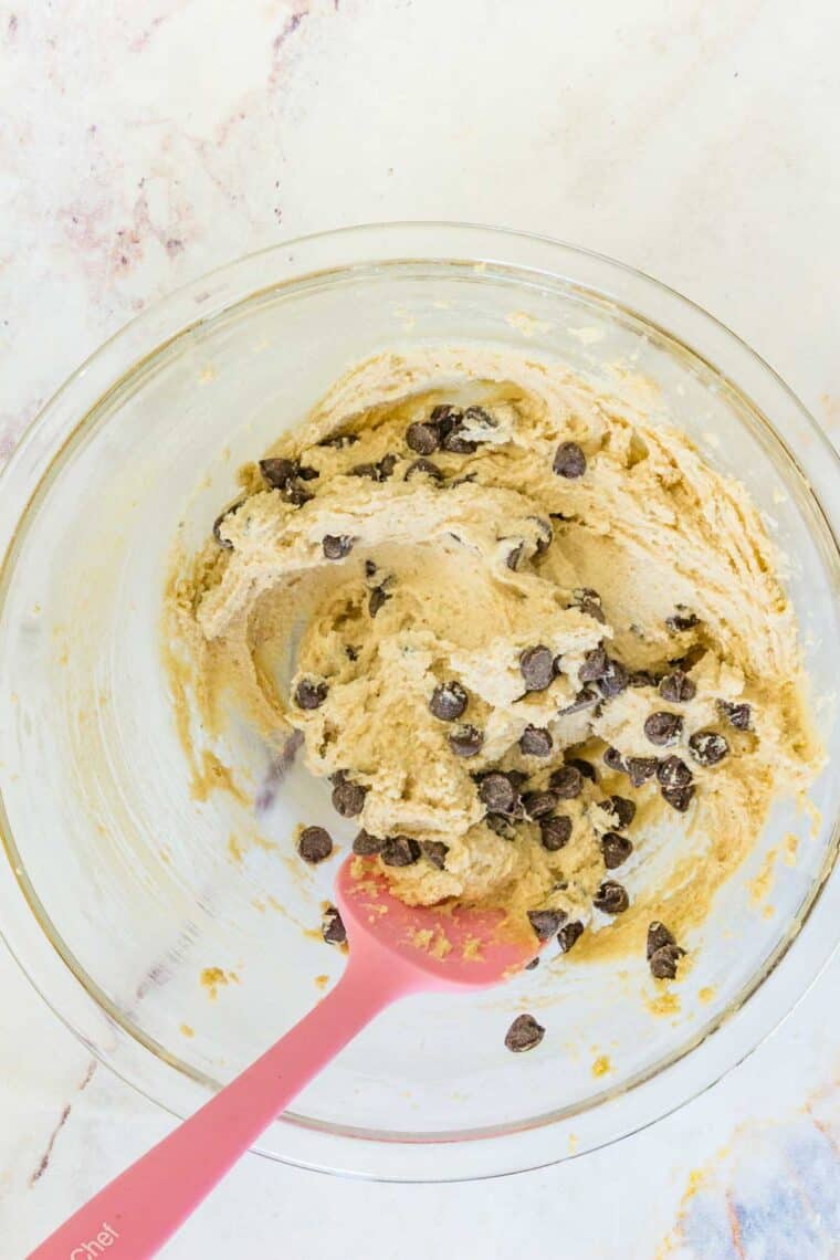 An easy recipe for edible chocolate chip cookie dough that's gluten-free and 100% safe to eat by the spoonful! The perfect sugary treat. Chocolate chips are stirred into gluten-free cookie dough with a pink spoon.