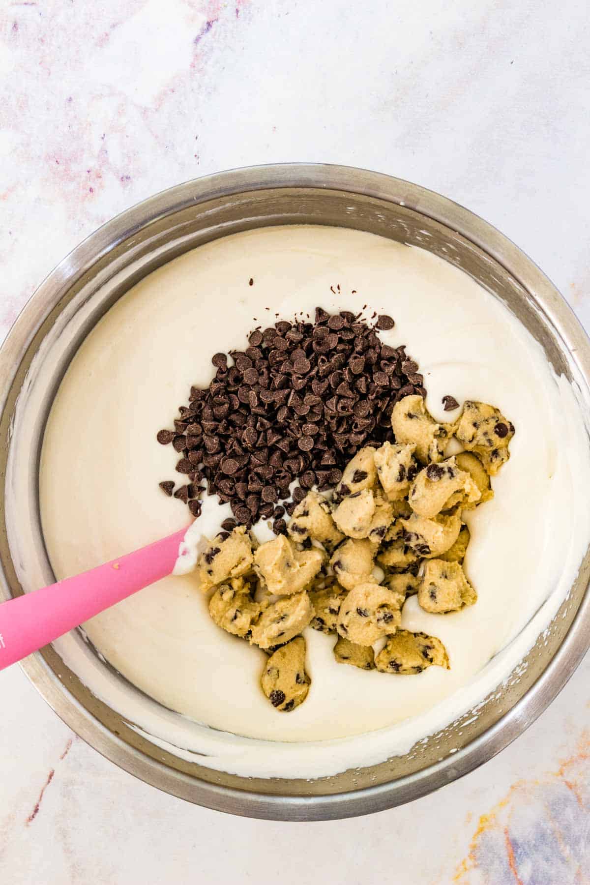 Chunks of chocolate chip cookie dough and chocolate chips added to a bowl with the vanilla ice cream base.