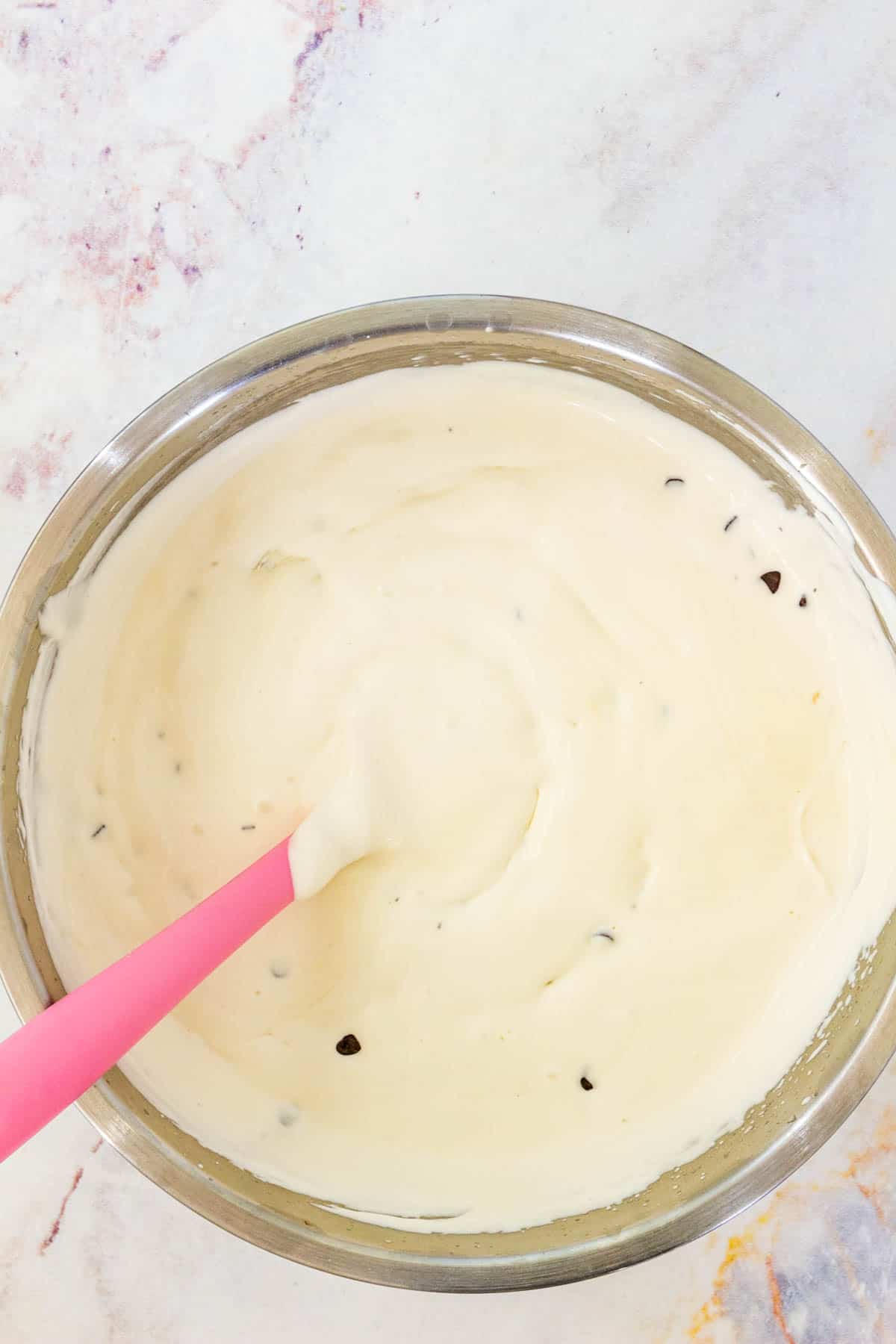 A mixing bowl full of chocolate chip cookie dough ice cream base with a pink spoon.