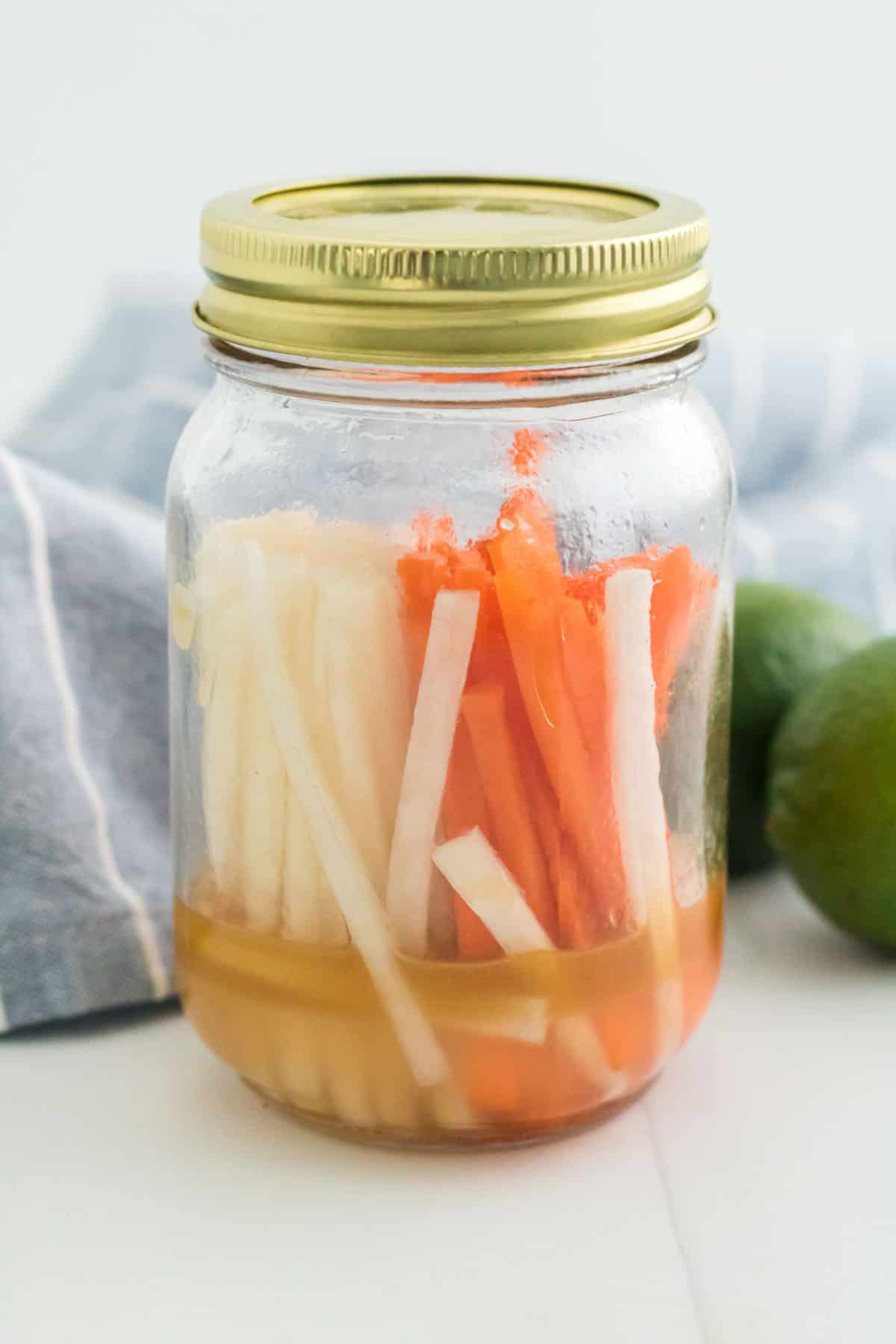 Julienned carrots and daikon radishes being pickled in a mason jar