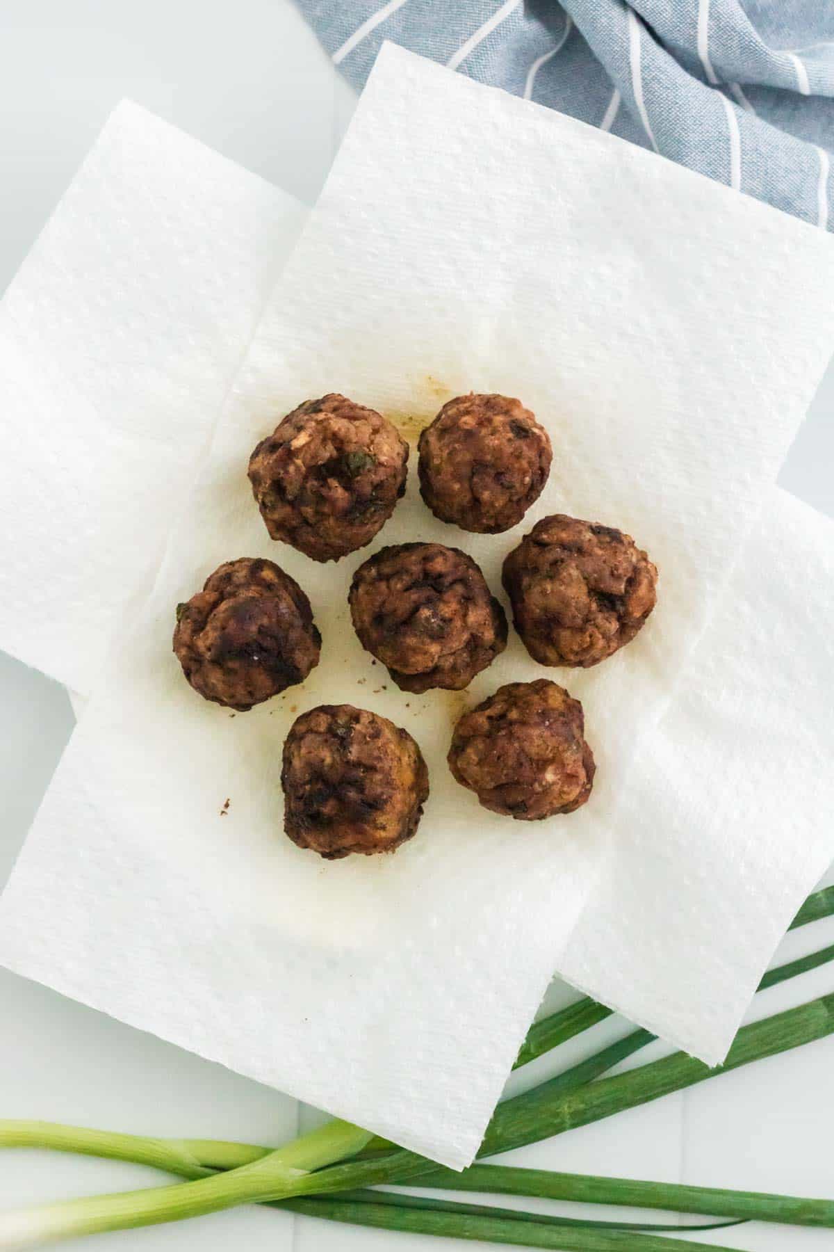 Seven fully cooked pork meatballs sitting on paper towels to drain