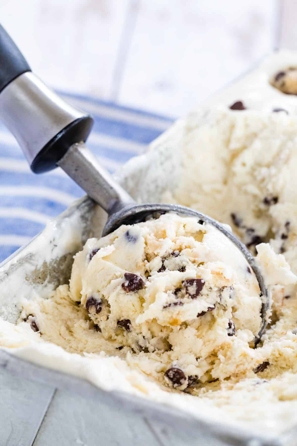 An ice cream scoop serves chocolate chip cookie dough no-churn ice cream from a metal loaf pan.