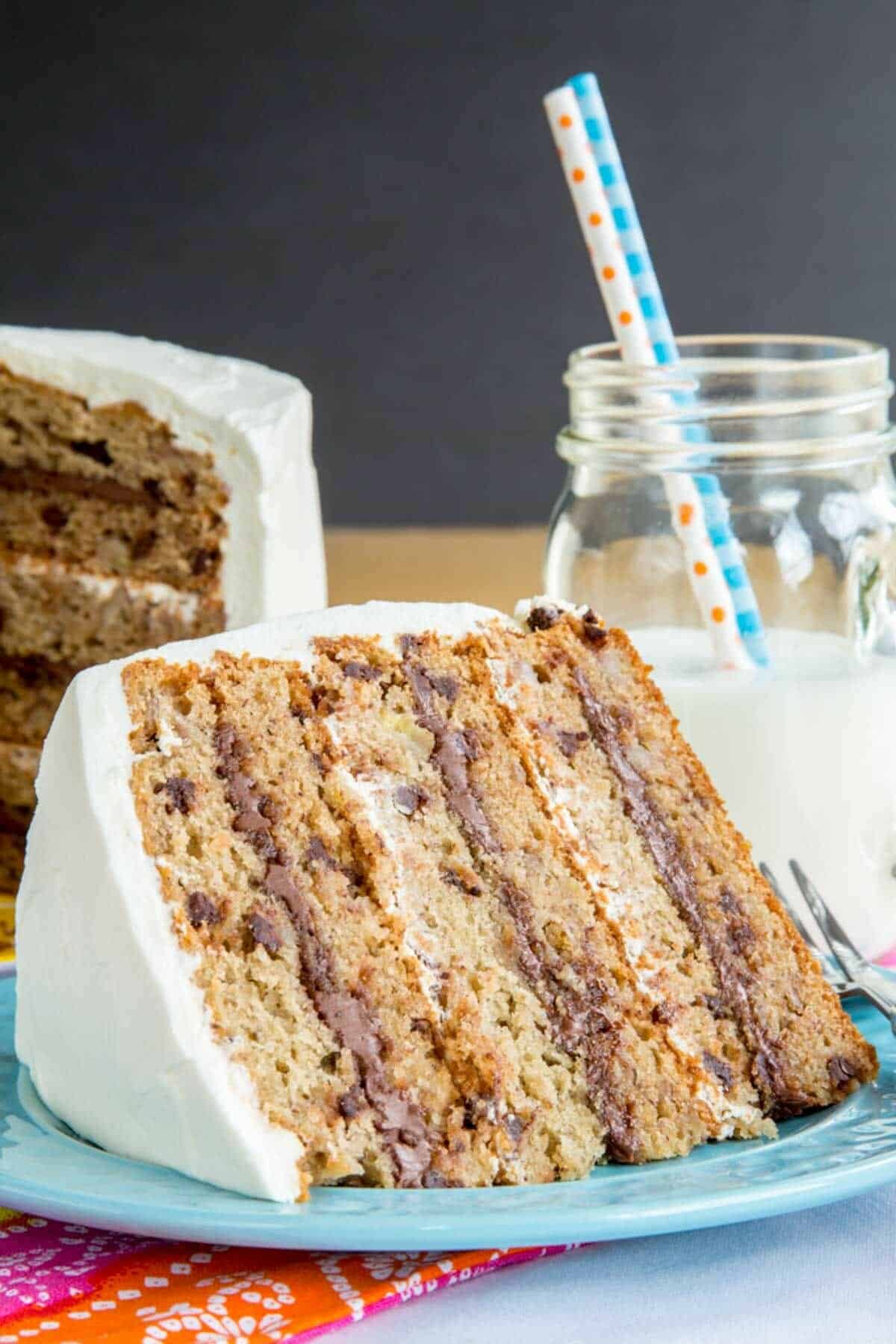 A slice of layered banana cake filled with Nutella and chocolate chips with a glass of milk in the background.