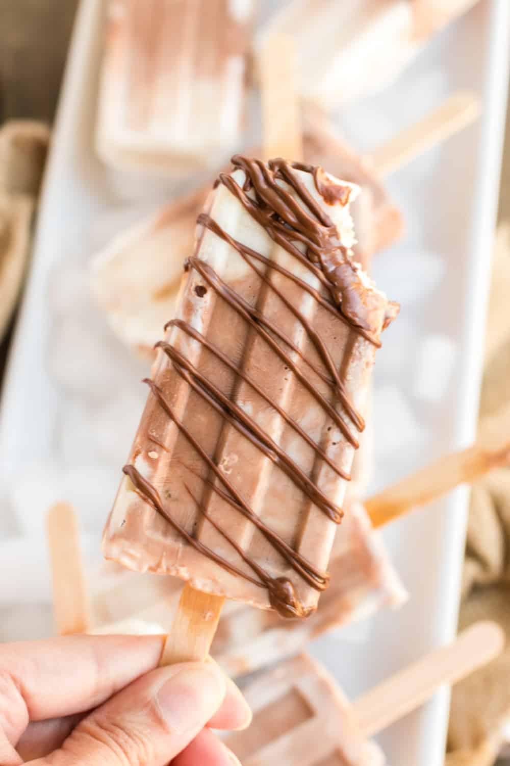 A swirled banana popsicle drizzled with Nutella with a bite taken out.