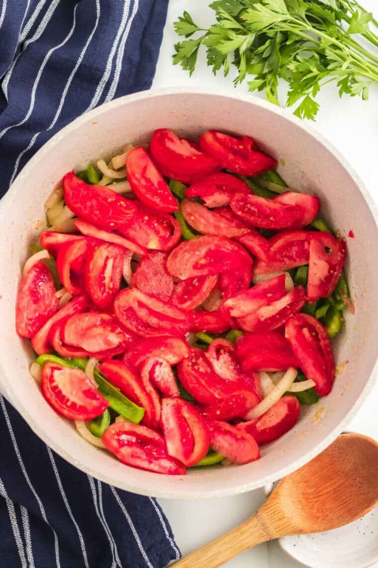 Tomatoes laid over the top of the pepper and onion slices in a cooking pot