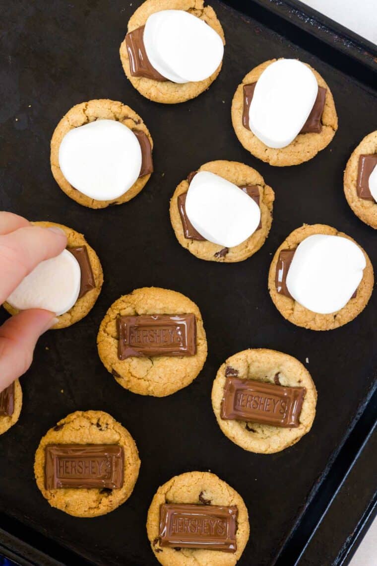 Marshmallows being placed on warm chocolate chip cookies with melted chocolate squares