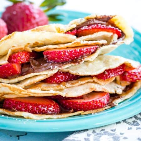 Folded crepes filled with strawberry slices and nutella on a turquoise-colored plate.