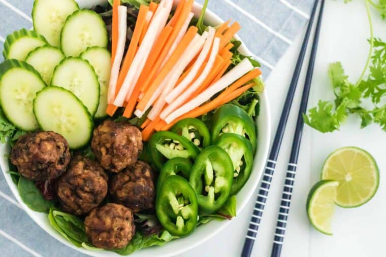 Banh mi salad with pork meatballs, julienned carrot and daikon radish pickles, jalapeño and cucumber slices beside a pair of chopsticks
