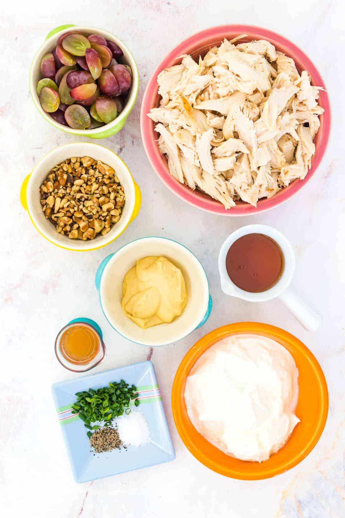 Bowls of chicken salad ingredients on a marble countertop.