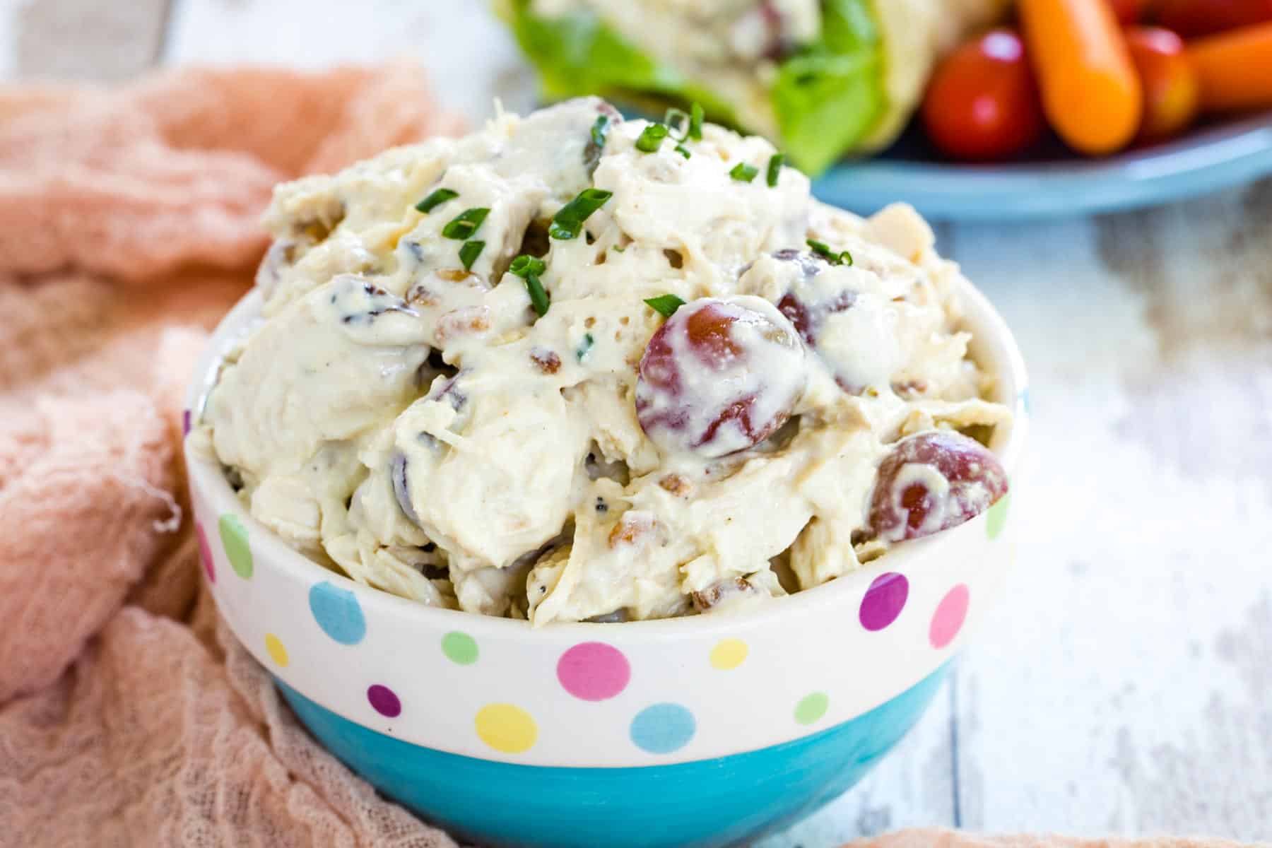 A decorative blue bowl filled with chicken salad garnished with chives.