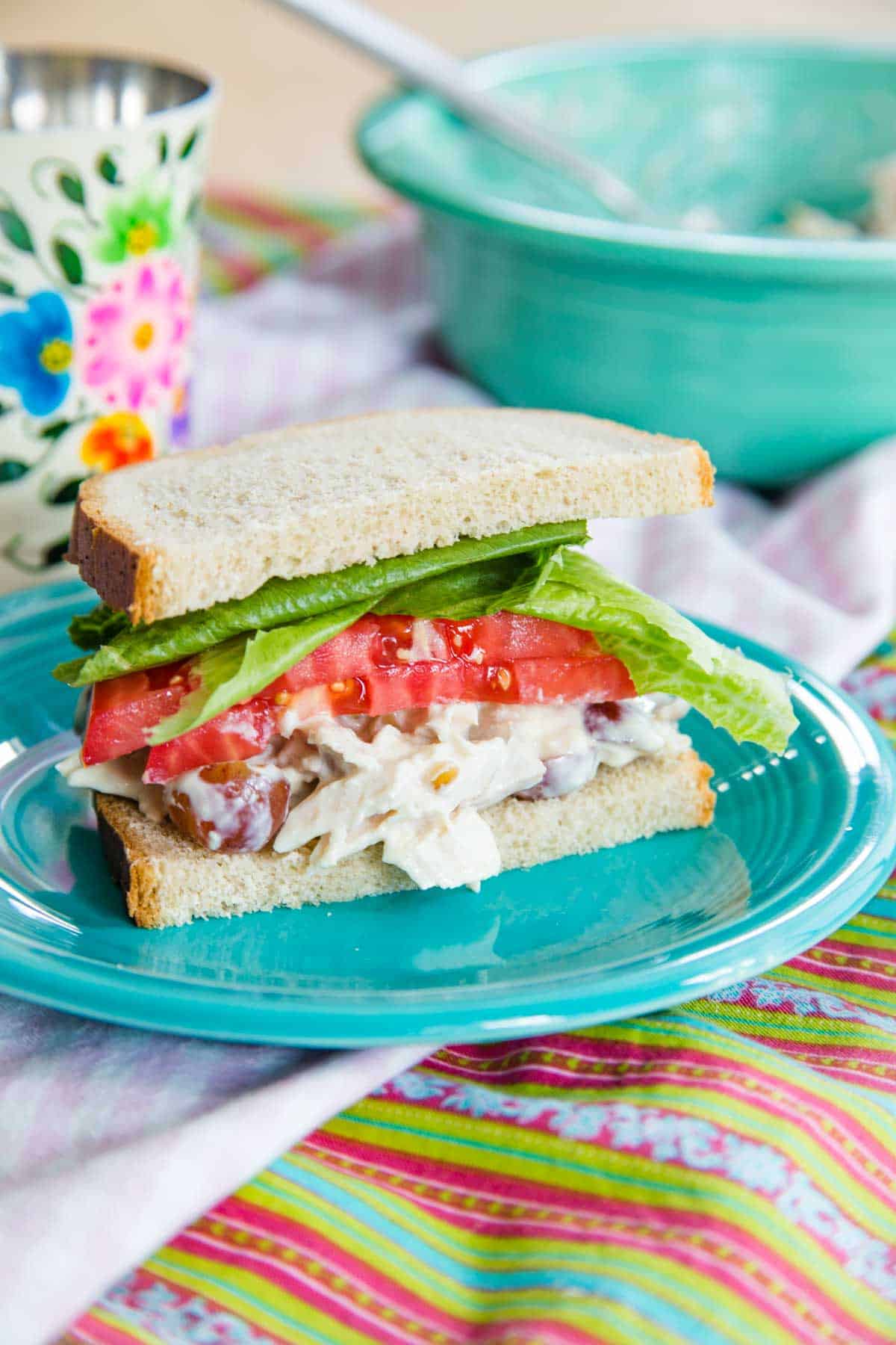 A chicken salad sandwich with lettuce and tomato on a turquoise plate on top of cloth napkins.