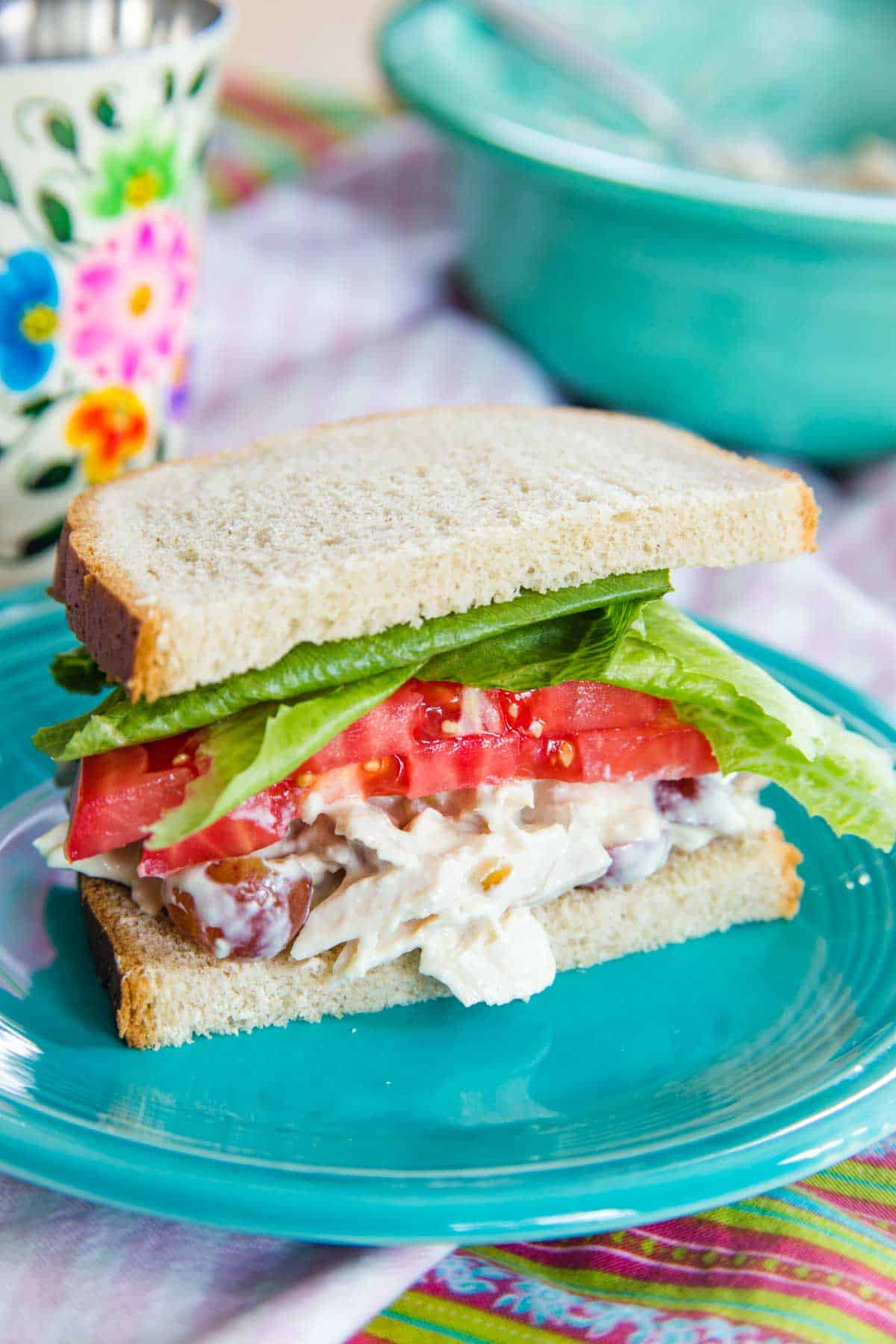Waldorf chicken salad between two slices of bread with lettuce and tomatoes on a plate.
