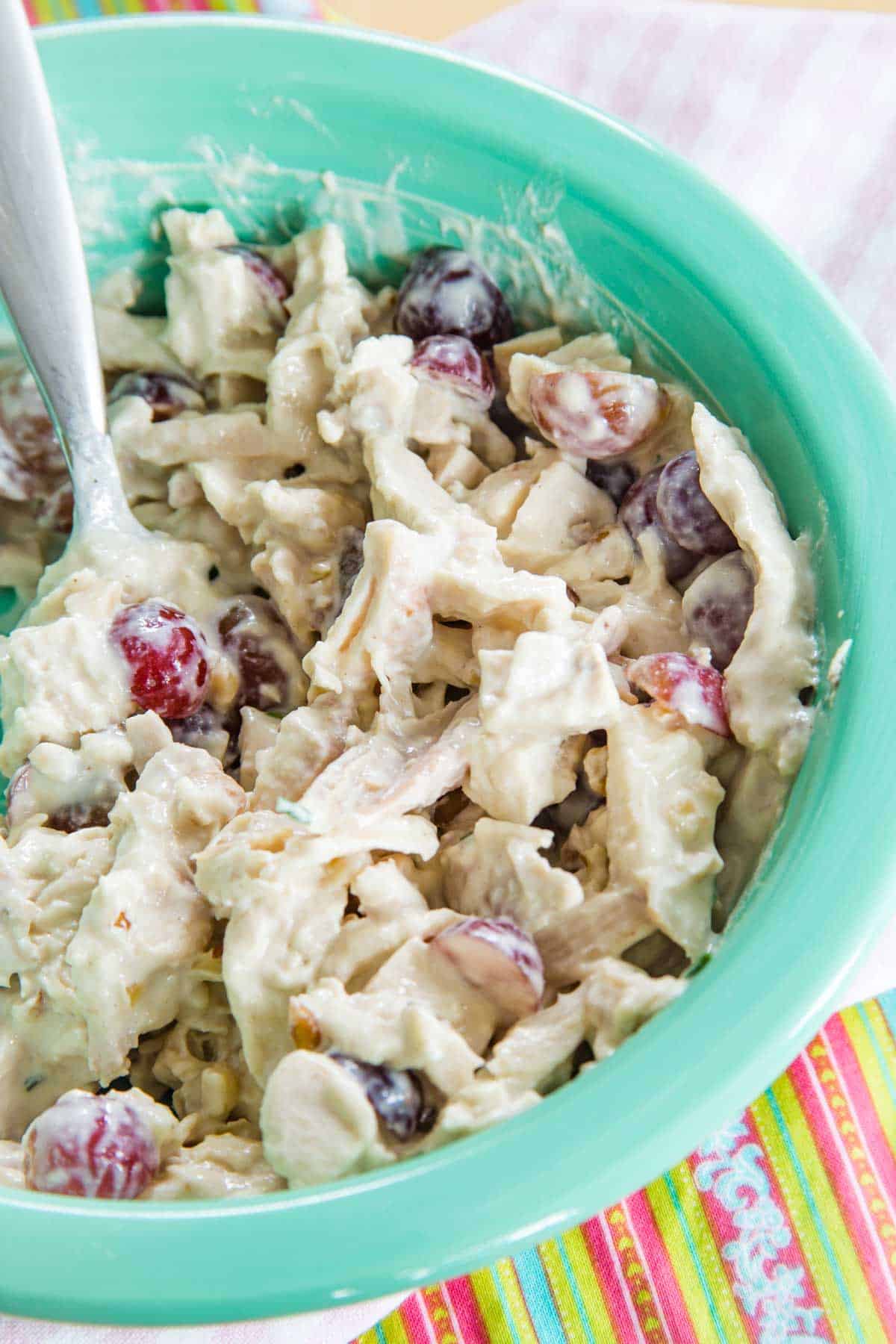 A large turquoise bowl filled with chicken salad with grapes and walnuts with a spoon in it.