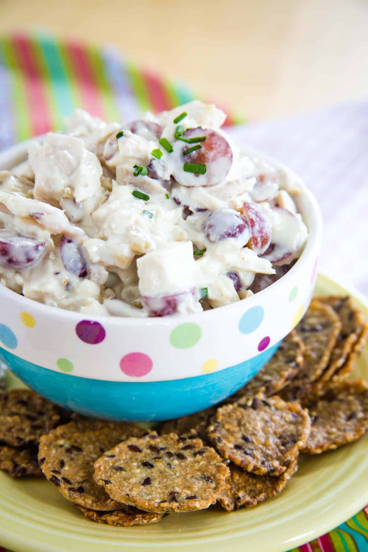 A bowl of chicken salad on a plate surrounded by crackers.