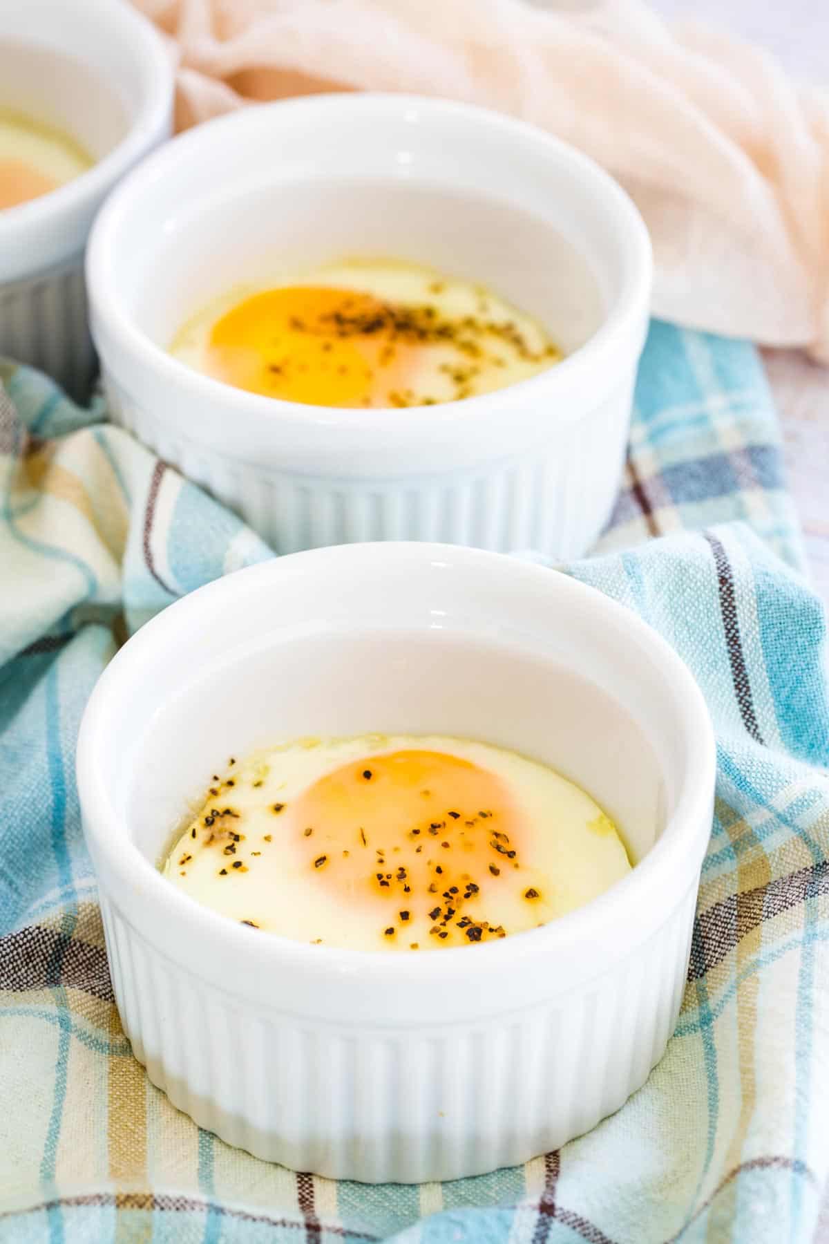 Two baked eggs seasoned with salt and pepper inside white ramekins.
