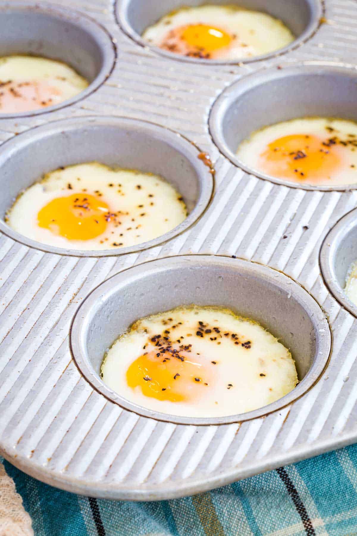 Seasoned baked eggs in the wells of a metal muffin pan.