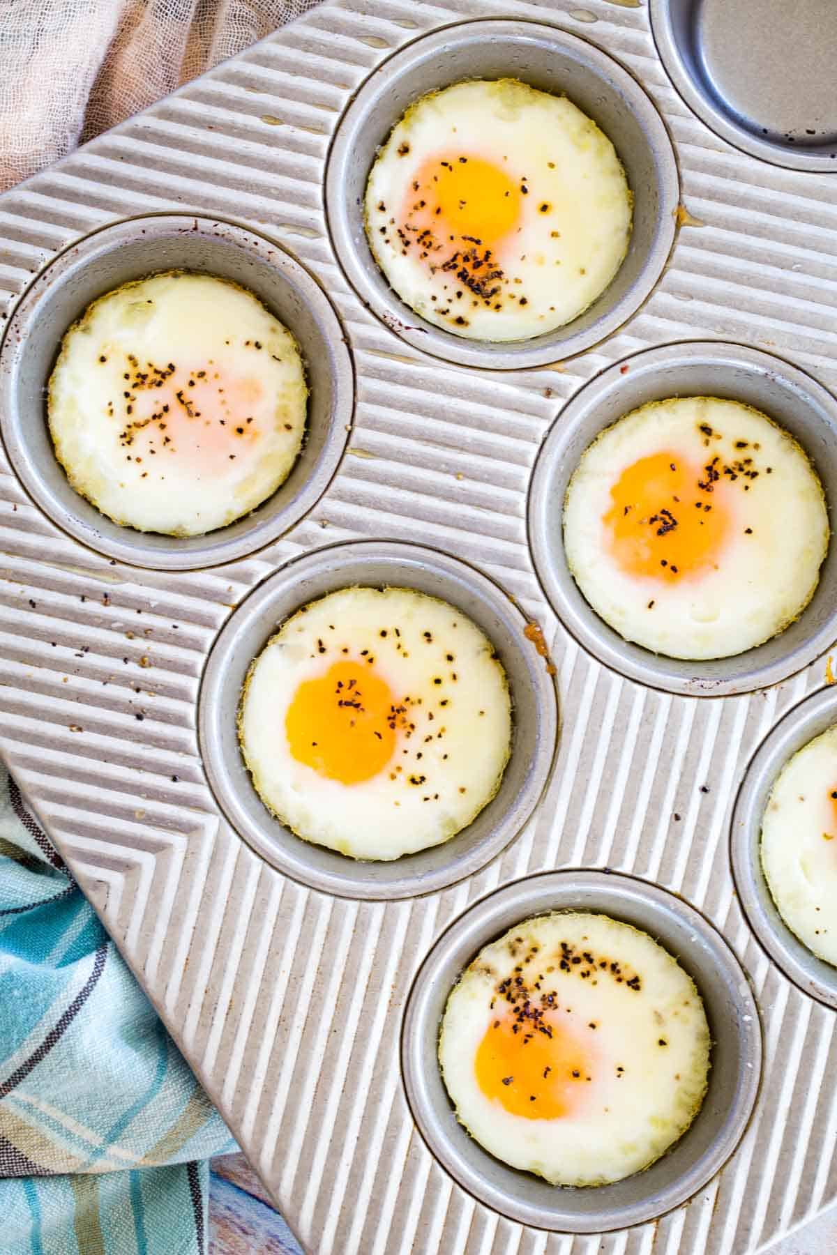 Top view of seasoned baked eggs in the wells of a metal muffin pan.