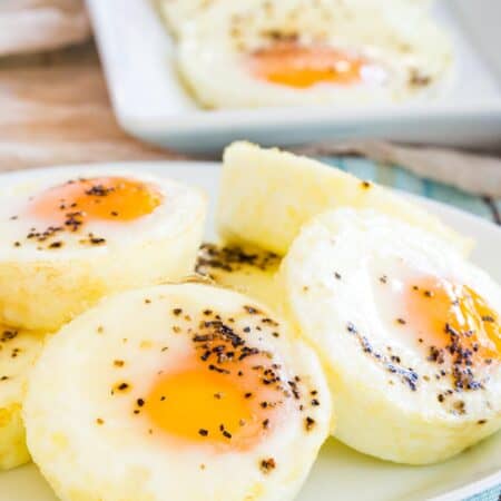 A plate of baked eggs seasoned with salt and pepper in the foreground, with a rectangular platter of baked eggs in the background.