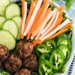 A bowl of salad topped with meatballs, pickled vegetables, and cucumber and jalapeno slices.