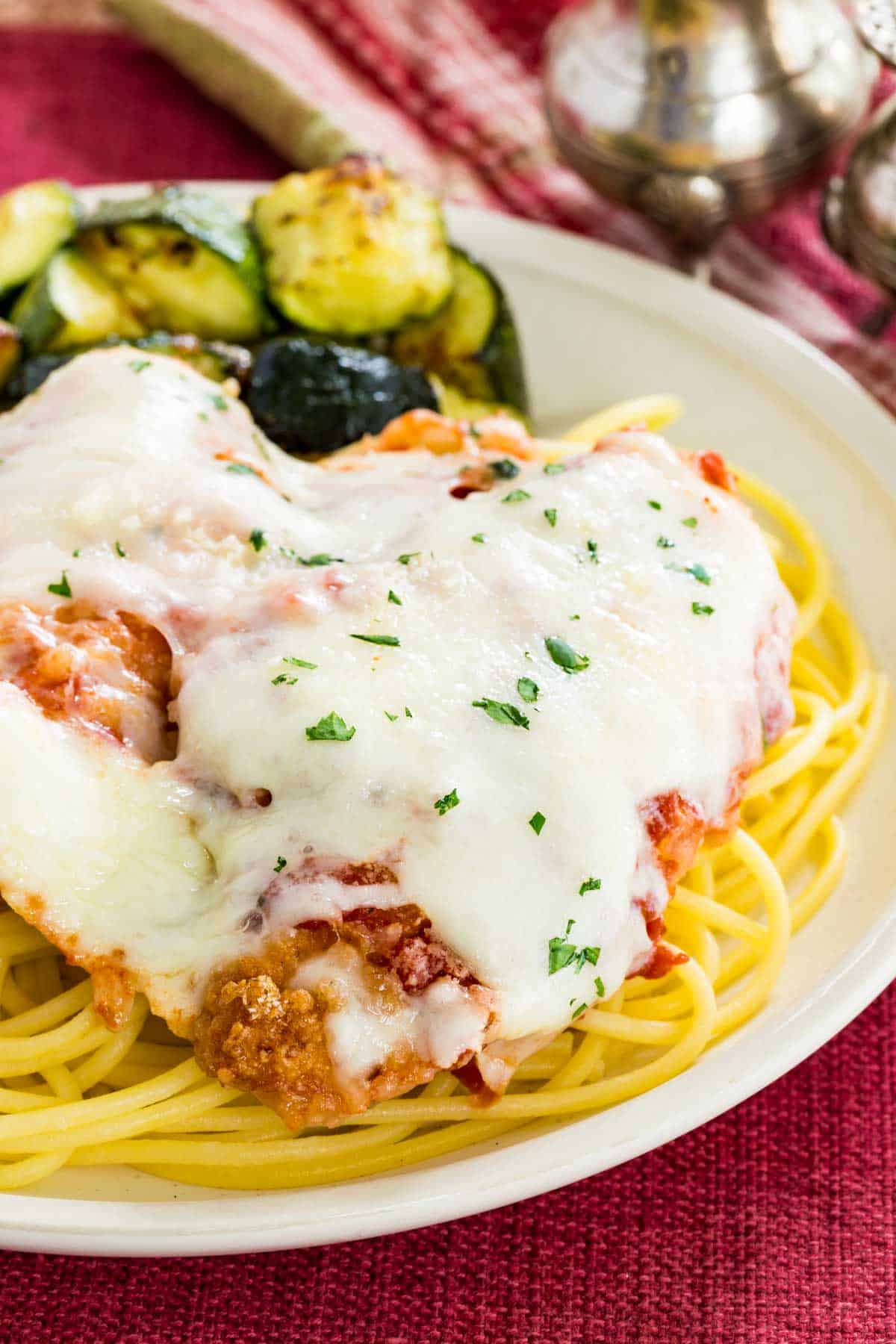 Gluten free chicken parmesan served over a plate of spaghetti with roasted zucchini on the side.