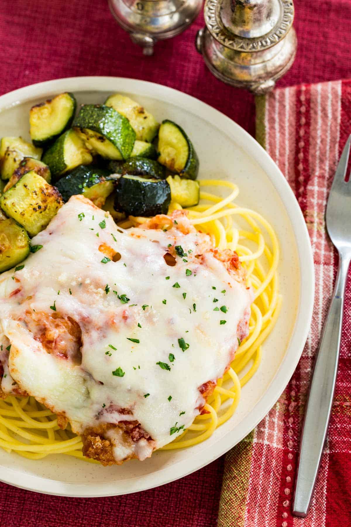 Top view of gluten free chicken parmesan served over a plate of spaghetti with roasted zucchini on the side.