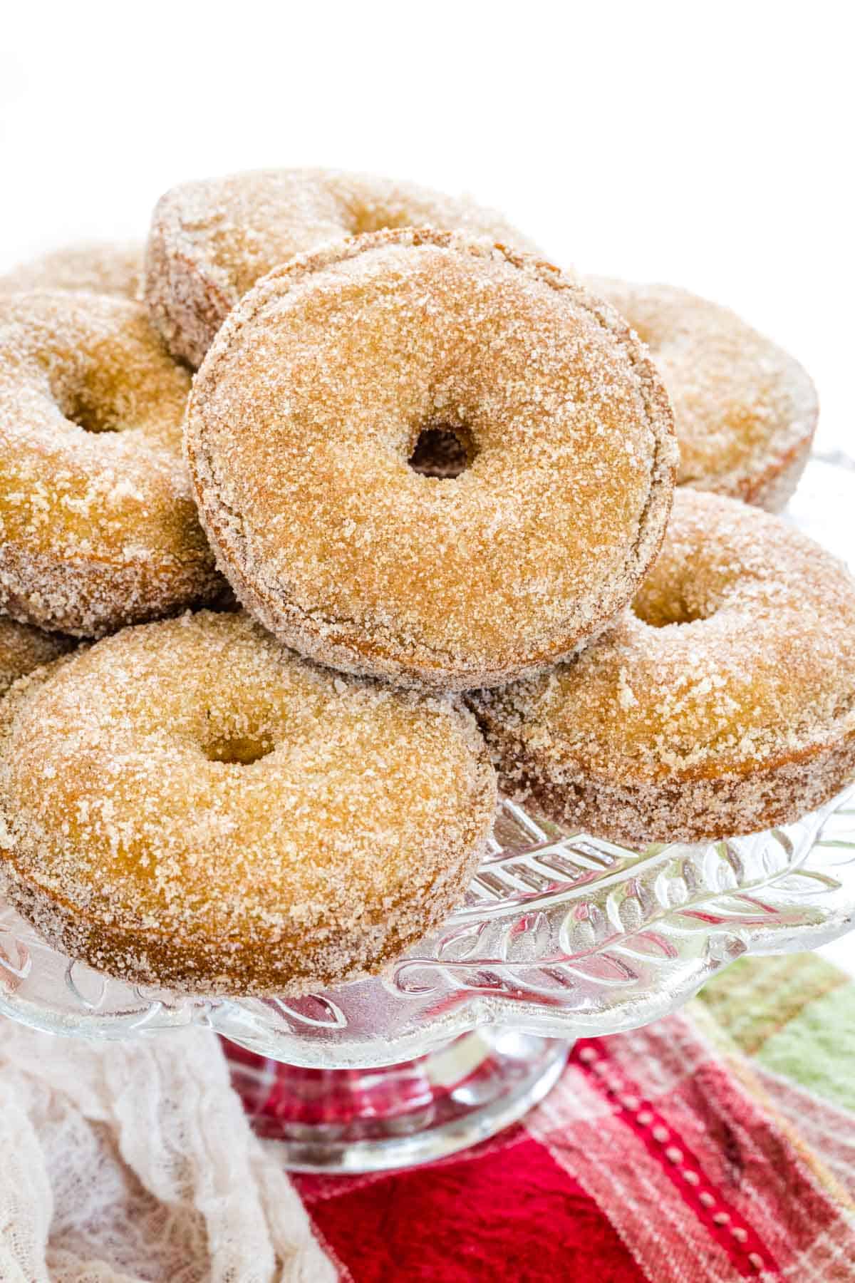 An assortment of gluten free apple cider donuts arranged on a large glass cake stand.