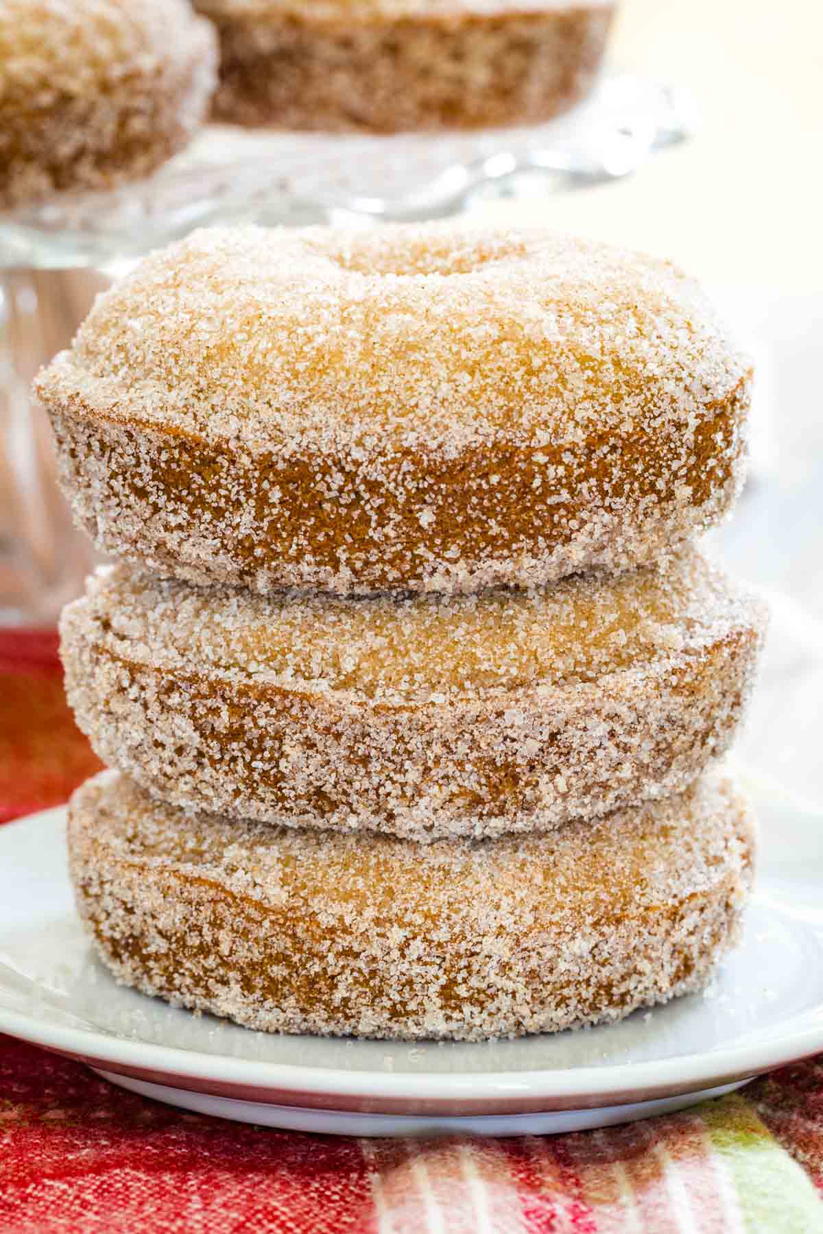 A stack of three gluten free apple cider donuts on a plate.