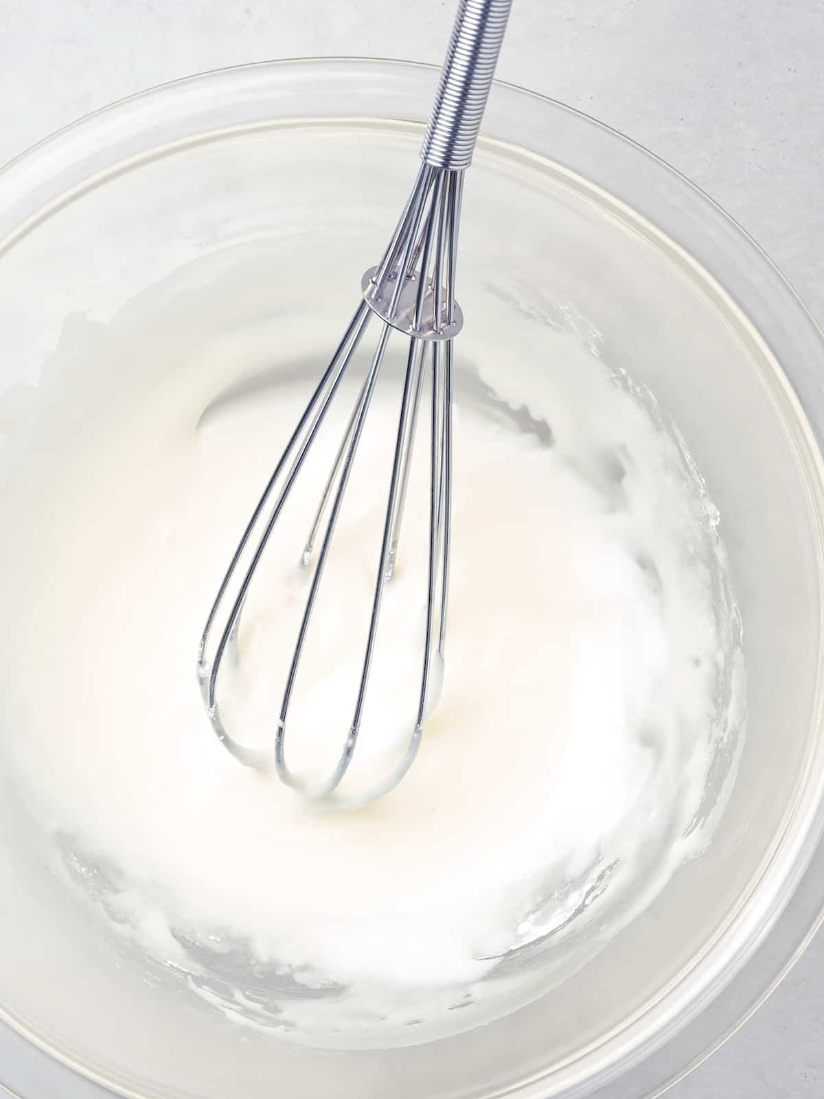 White sweet glaze in a clear mixing bowl with a whisk.