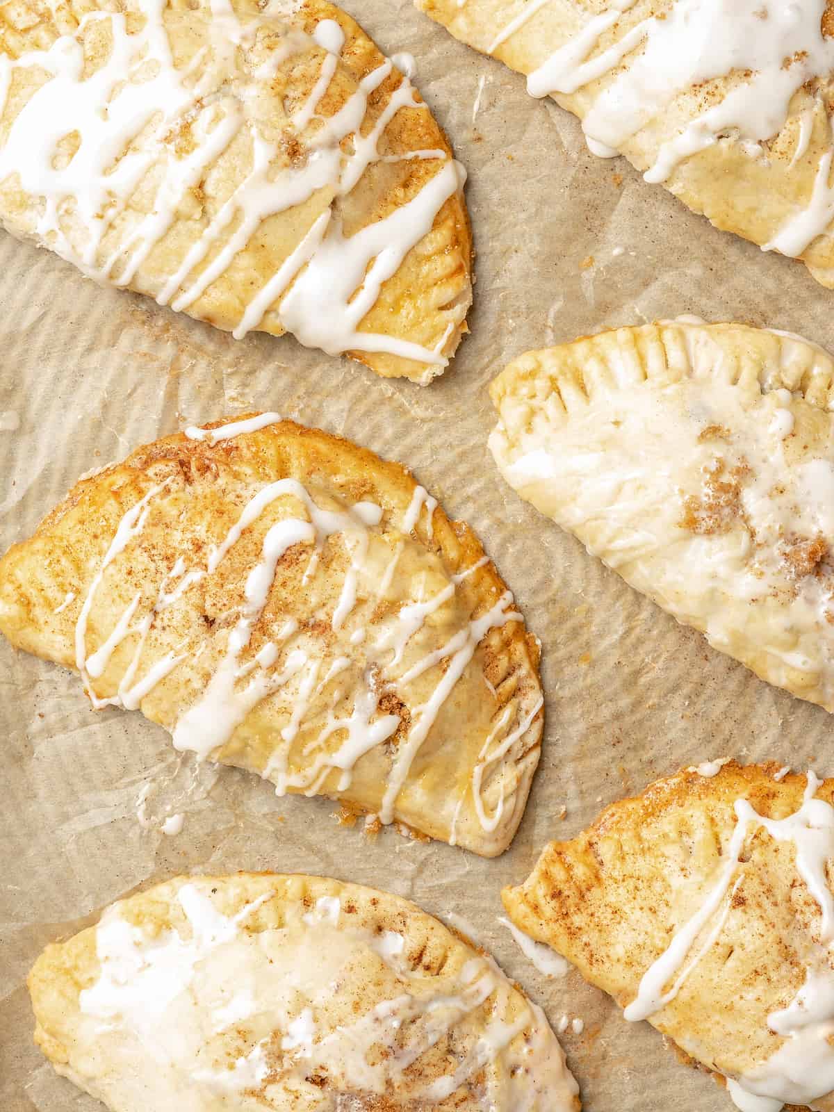 Rows of apple turnovers on parchment paper, drizzled with sweet glaze.