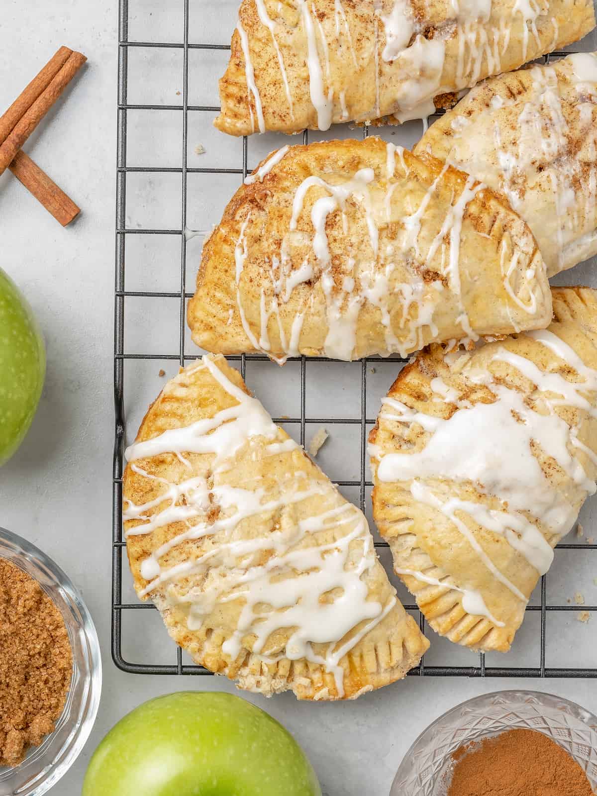 Glazed apple turnovers on a black wire rack, next to green Granny Smith apples.