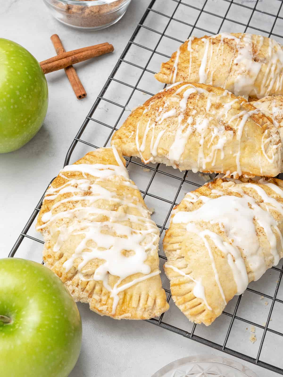 Glazed apple turnovers on a black wire rack, next to green Granny Smith apples.