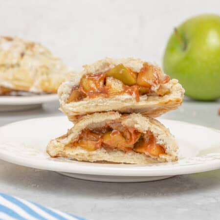 Two gluten free apple turnovers stacked on a white plate, revealing the apple filling.